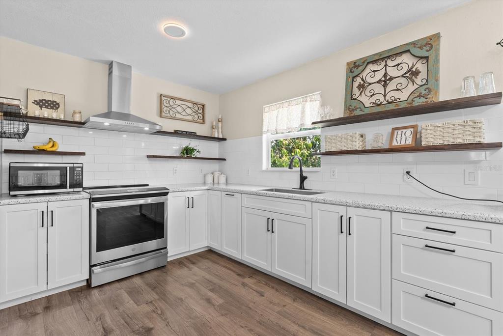 A kitchen with white cabinets, stainless steel appliances, open shelving, and white subway tile backsplash — 2600 CHARLENE STREET, PUNTA GORDA, FL