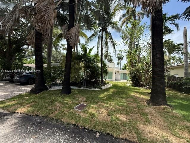 A low-slung house is partially obscured by palm trees and landscaping in a residential yard — 1047 NE 84th St, Miami FL 33138, MIAMI, FL