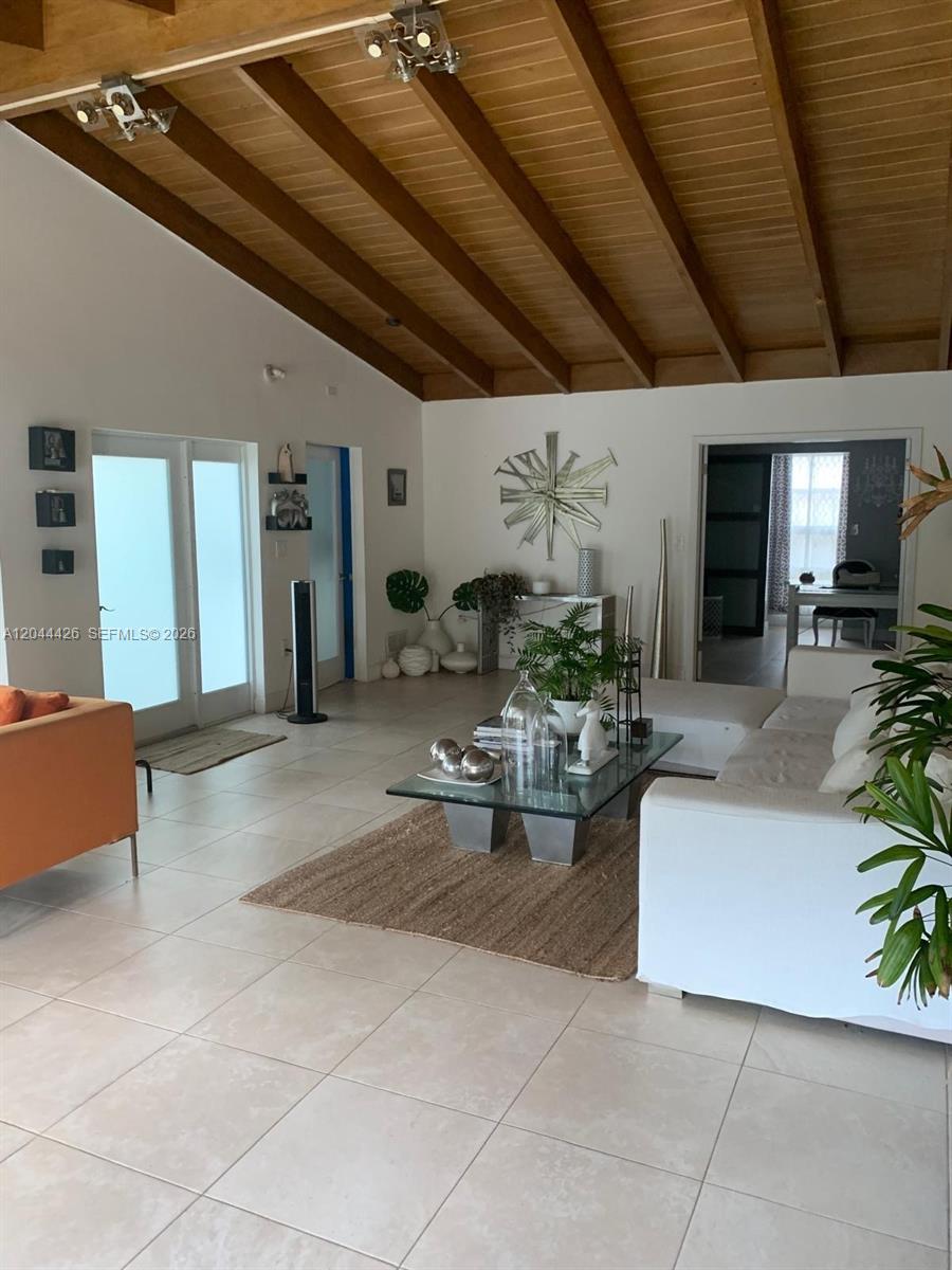 A living room features a vaulted wood-beam ceiling, tile flooring, and a white sectional sofa — 1047 NE 84th St, Miami FL 33138, MIAMI, FL