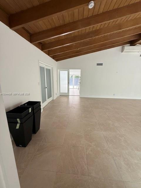 A spacious room features light tile flooring, a vaulted wood-beamed ceiling, and glass-paned doors — 1047 NE 84th St, Miami FL 33138, MIAMI, FL