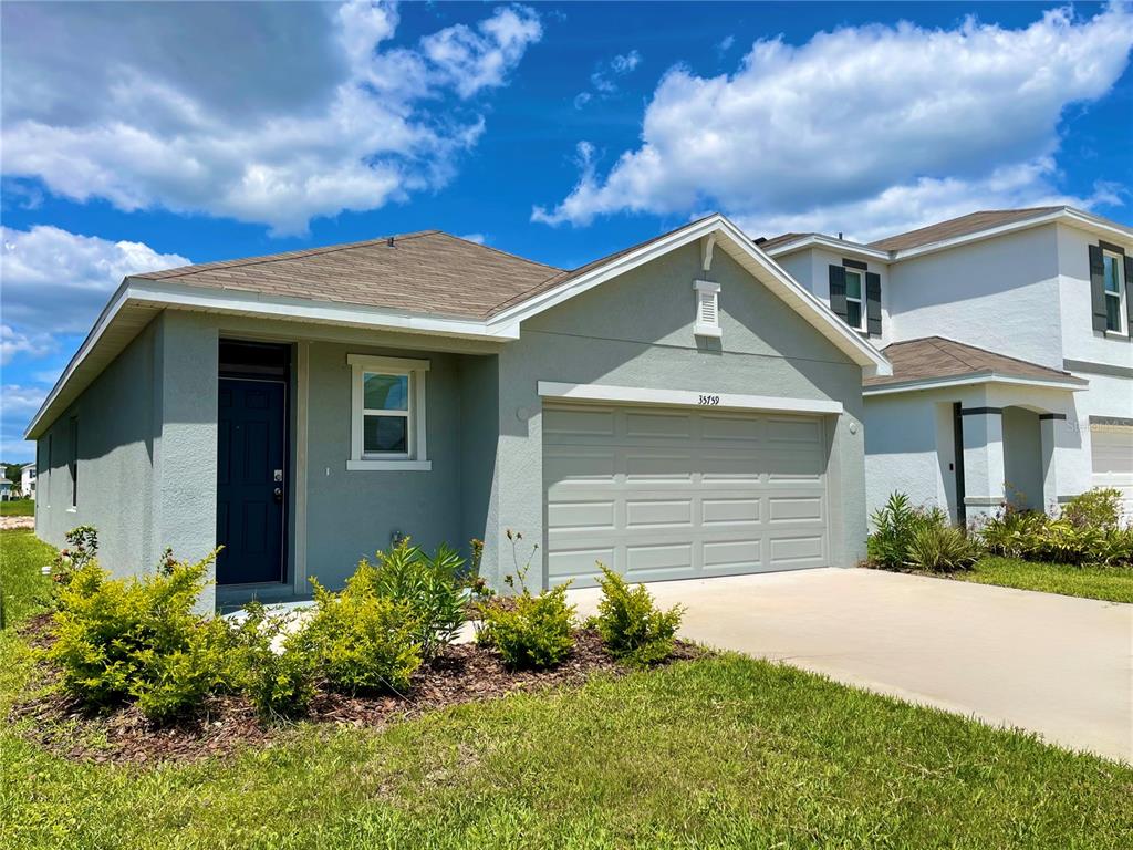 A single-story house with a light green stucco exterior, a two-car garage, and a driveway — 35759 SUNFLOWER HILL DR, ZEPHYRHILLS, FL