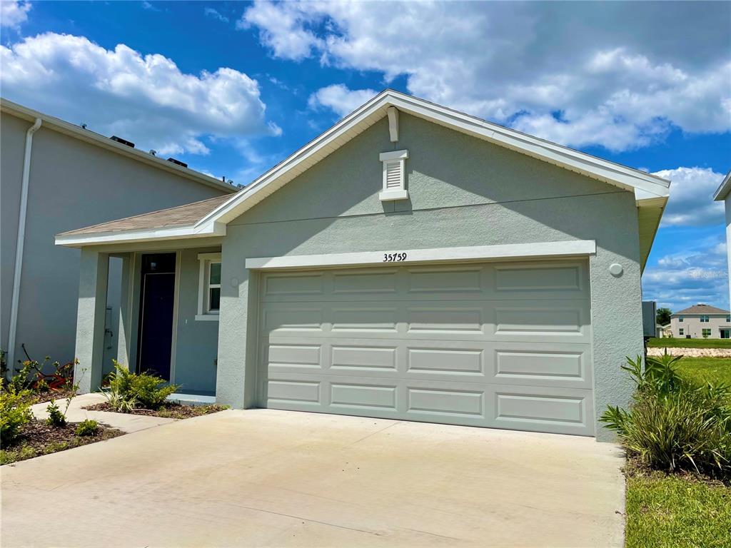 A light green single-story house features a two-car garage and a covered entryway — 35759 SUNFLOWER HILL DR, ZEPHYRHILLS, FL
