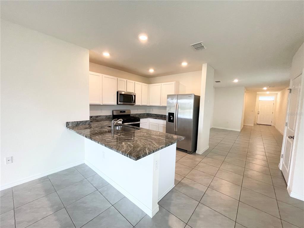 A kitchen features white cabinets, granite countertops, stainless steel appliances, and light-colored tile flooring — 35759 SUNFLOWER HILL DR, ZEPHYRHILLS, FL
