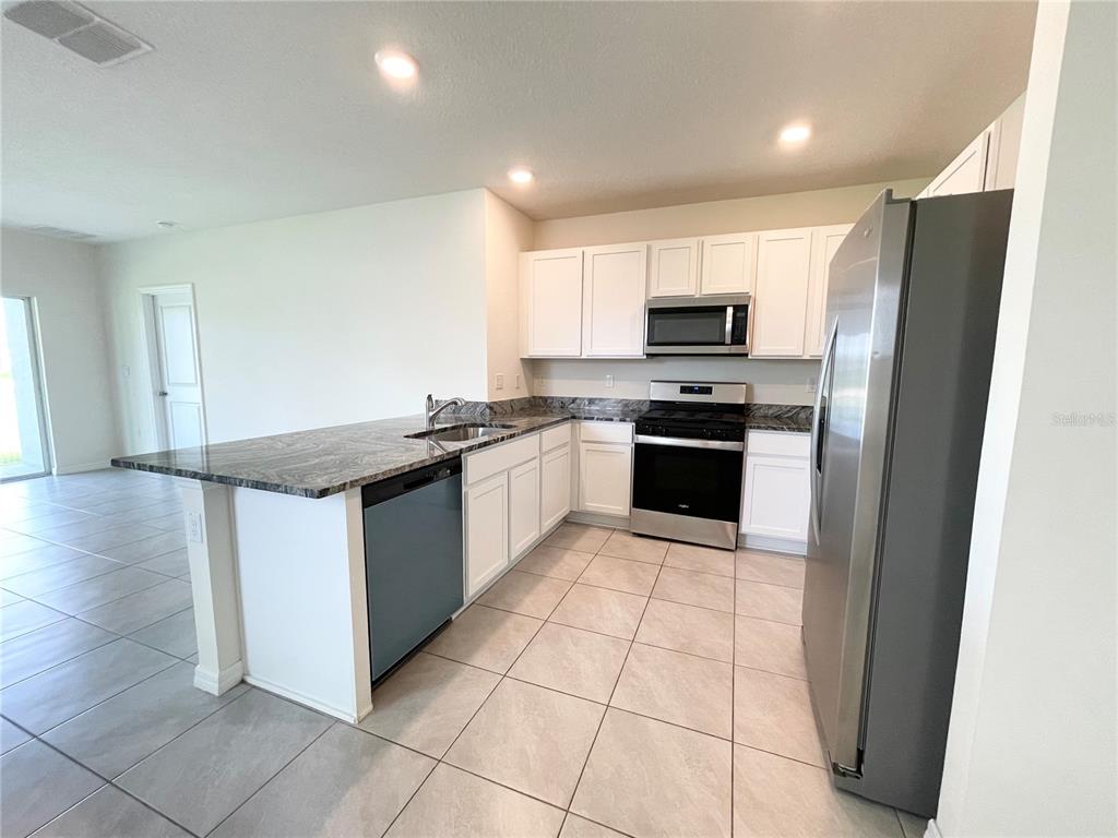 A kitchen features white cabinets, granite countertops, stainless steel appliances, and light tile flooring — 35759 SUNFLOWER HILL DR, ZEPHYRHILLS, FL
