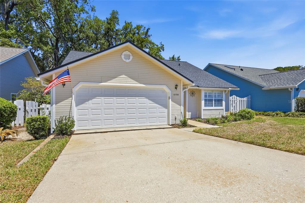 A beige single-story house with a two-car garage and an American flag on the front — 10530 NW 36TH LANE, GAINESVILLE, FL