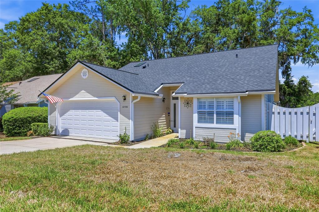 A single-story house with beige siding, a white garage door, and a dark shingled roof — 10530 NW 36TH LANE, GAINESVILLE, FL