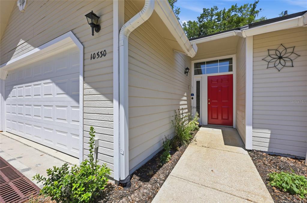 The exterior of a house features beige siding, a white garage door, and a red door — 10530 NW 36TH LANE, GAINESVILLE, FL