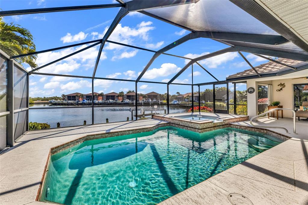 A screened-in pool and spa overlook a canal with docked boats under a blue sky — 3518 TERIN COURT, PUNTA GORDA, FL