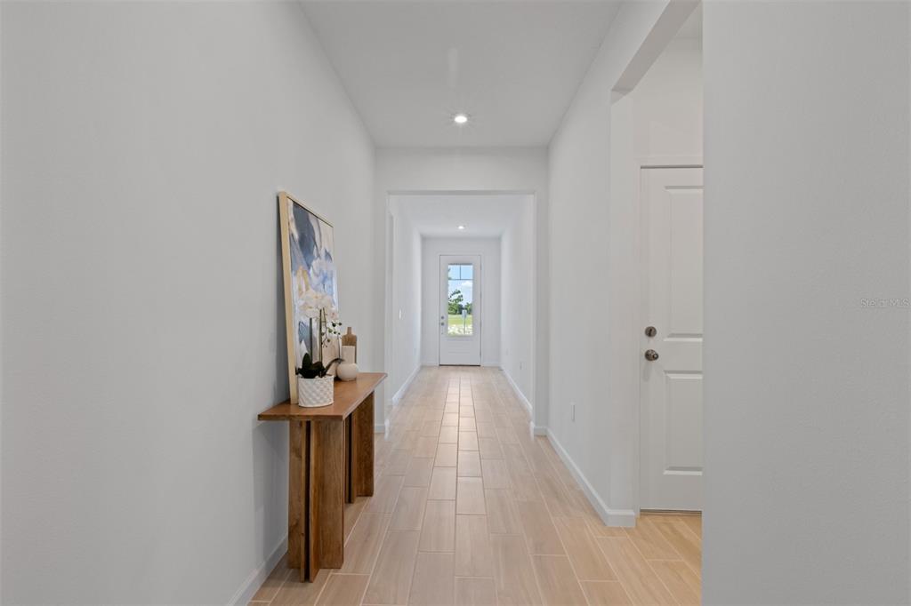 A long, narrow hallway features light-colored wood-look tile flooring and a wooden console table — 2612 GINSENG IVY STREET, APOPKA, FL