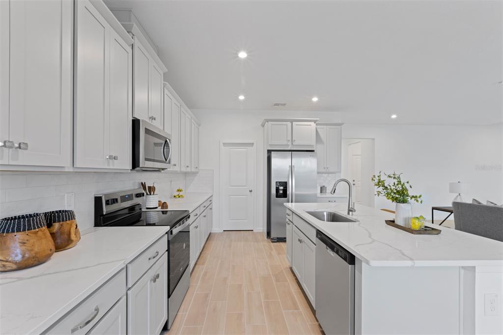 A modern kitchen features white cabinetry, stainless steel appliances, and a quartz-topped island — 2612 GINSENG IVY STREET, APOPKA, FL