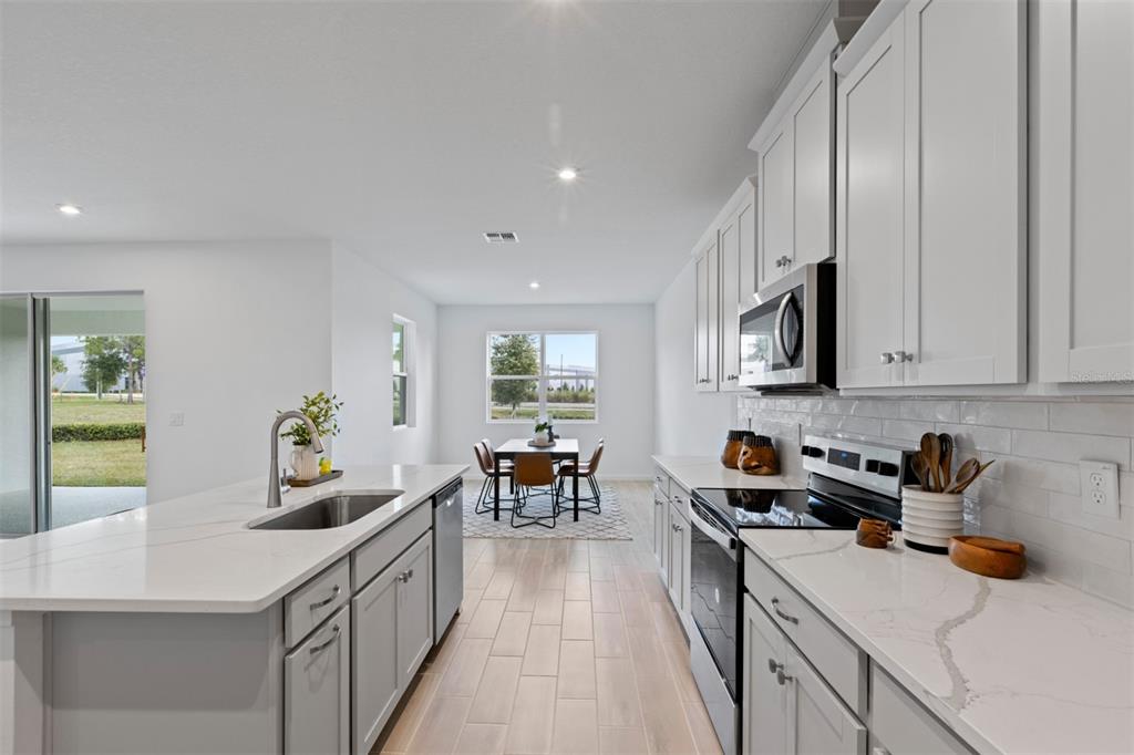A modern kitchen with white cabinets, quartz countertops, and a dining area in the background — 2612 GINSENG IVY STREET, APOPKA, FL