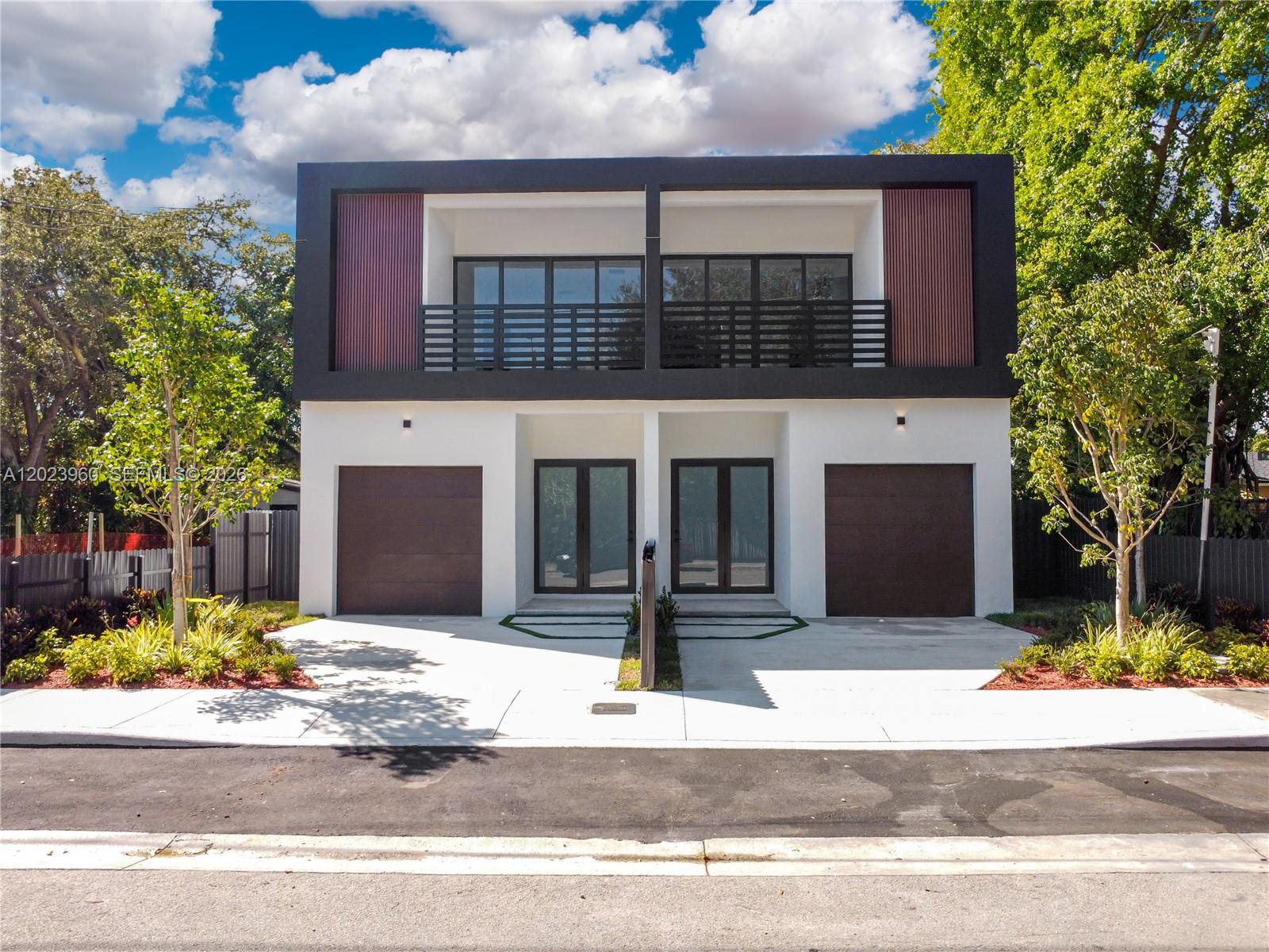 A modern two-story duplex features white stucco walls, dark wood garage doors, and upper-level balconies — 5116 NW 3rd Ave, Miami FL 33127, MIAMI, FL