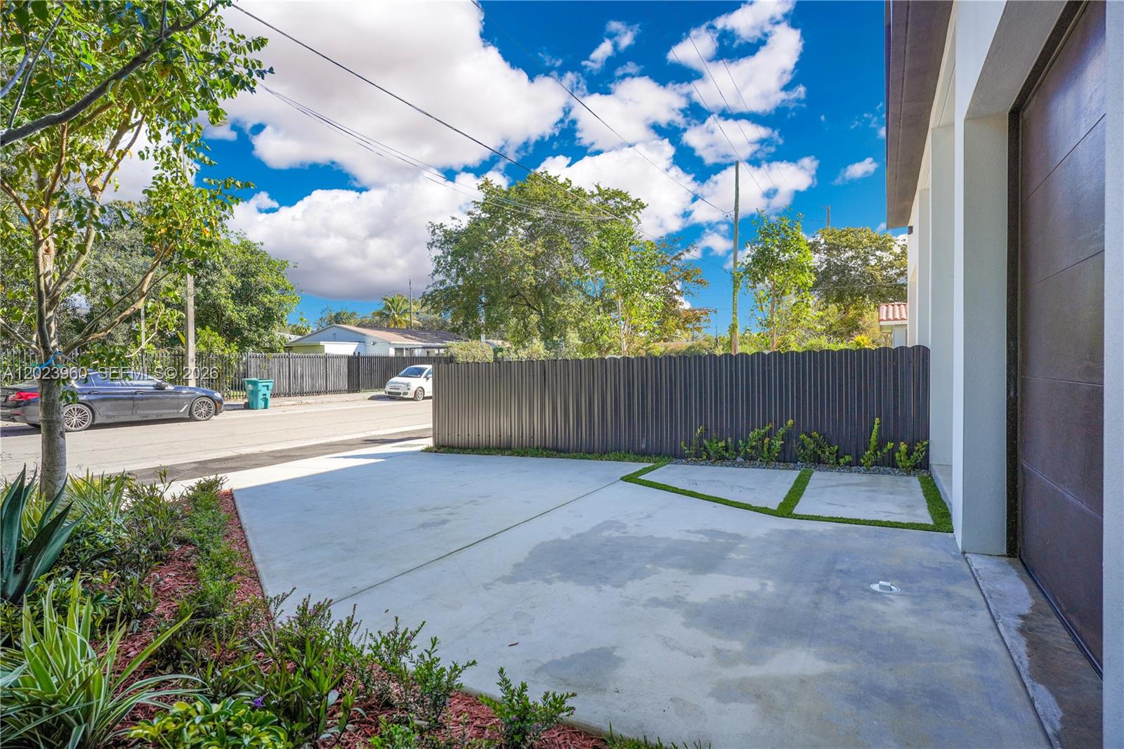 A concrete driveway leads to a modern garage door beside a dark metal privacy fence — 5116 NW 3rd Ave, Miami FL 33127, MIAMI, FL