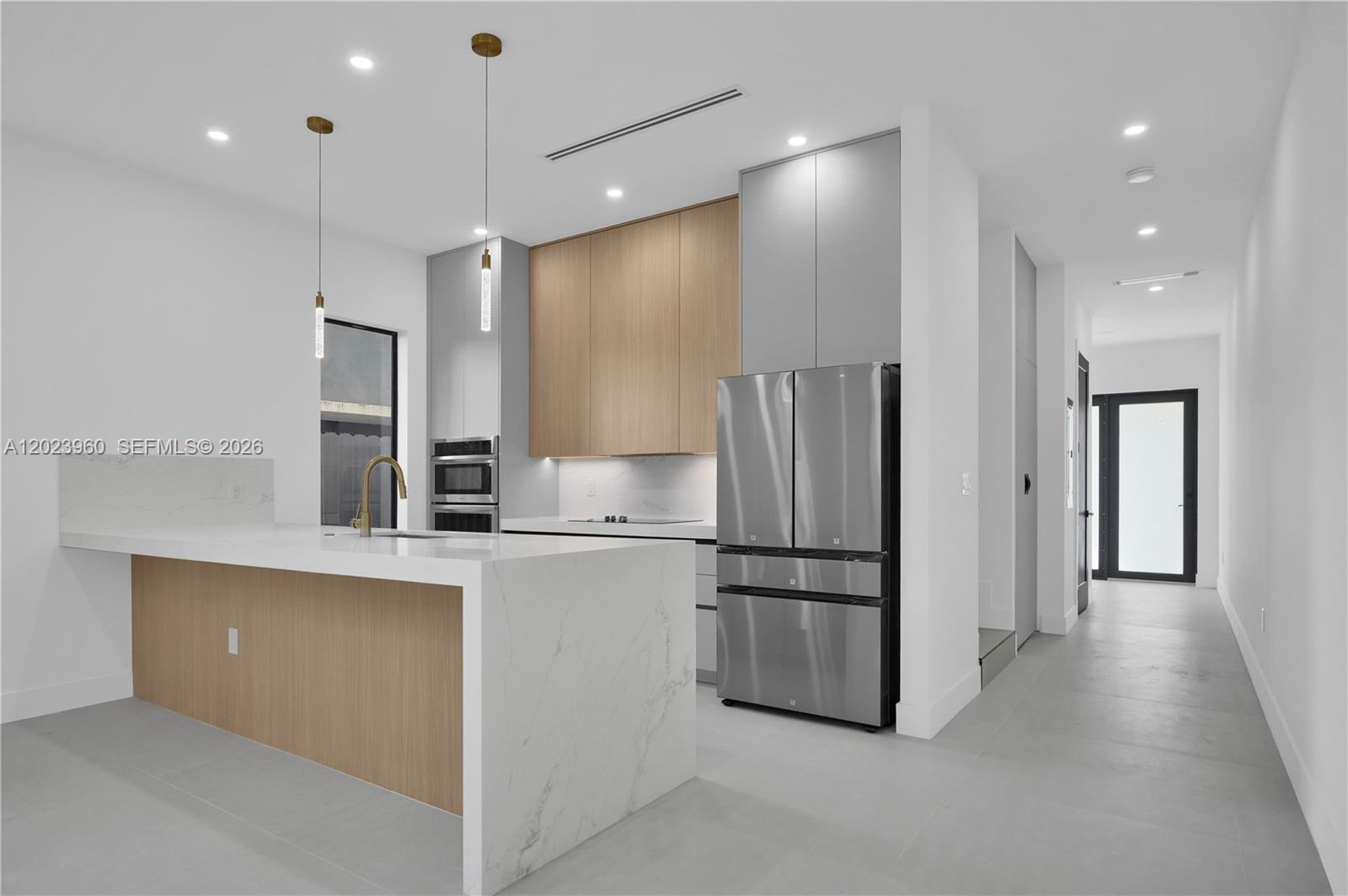 A modern kitchen features a marble waterfall island, light wood cabinetry, and stainless steel appliances — 5116 NW 3rd Ave, Miami FL 33127, MIAMI, FL