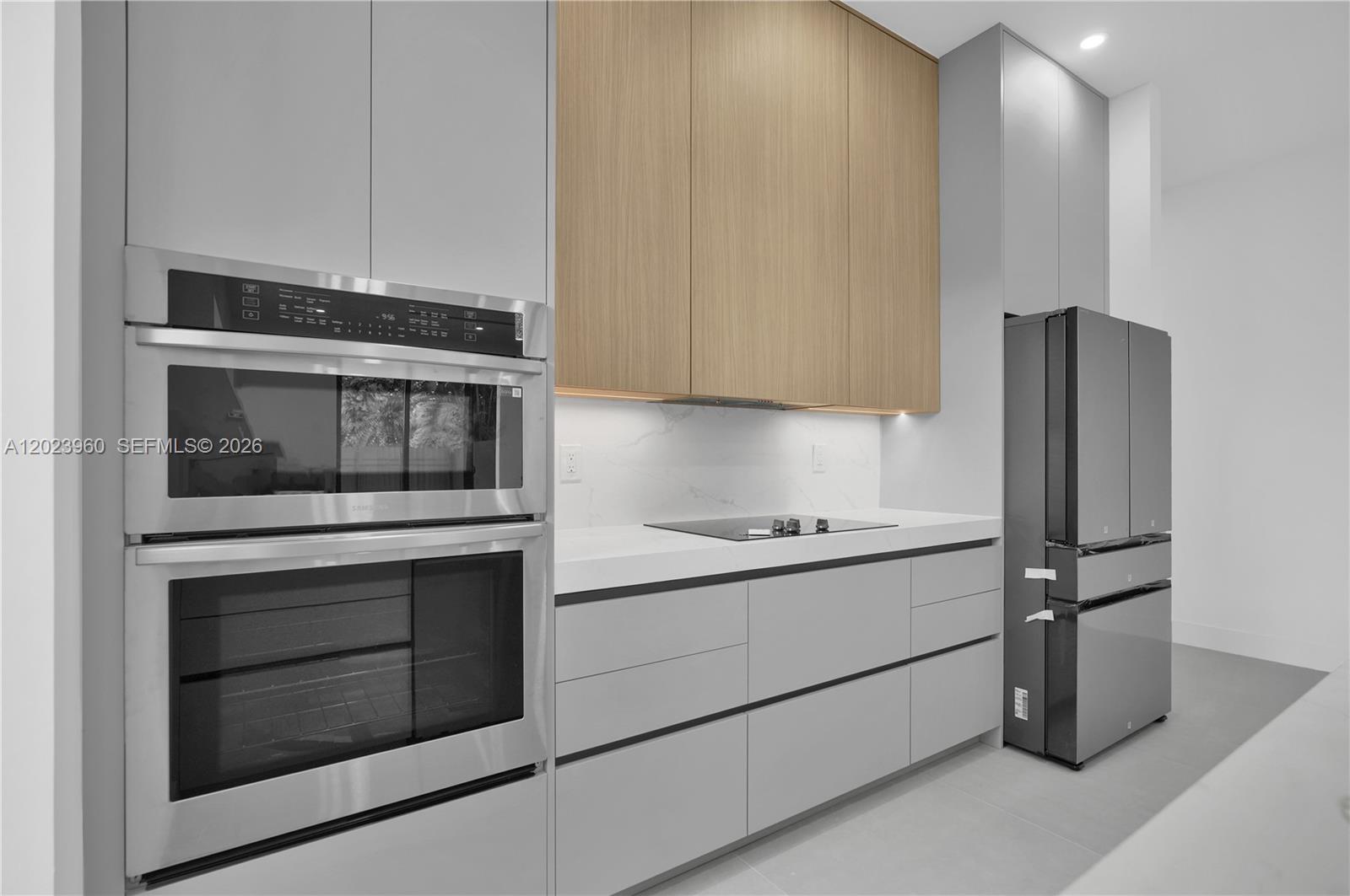 A modern kitchen features light gray cabinetry, wood-toned upper cabinets, stainless steel appliances, and countertops — 5116 NW 3rd Ave, Miami FL 33127, MIAMI, FL