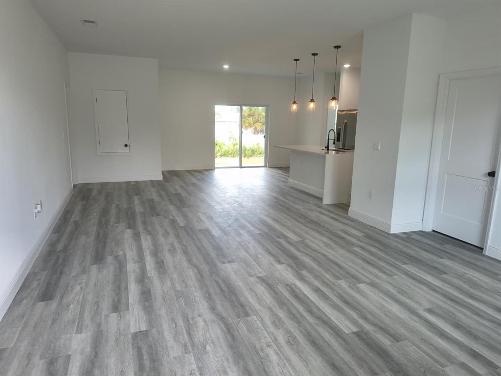 An open-concept living area features light gray wood-look flooring, white walls, and a kitchen island — 171 MARION OAKS TRAIL, OCALA, FL