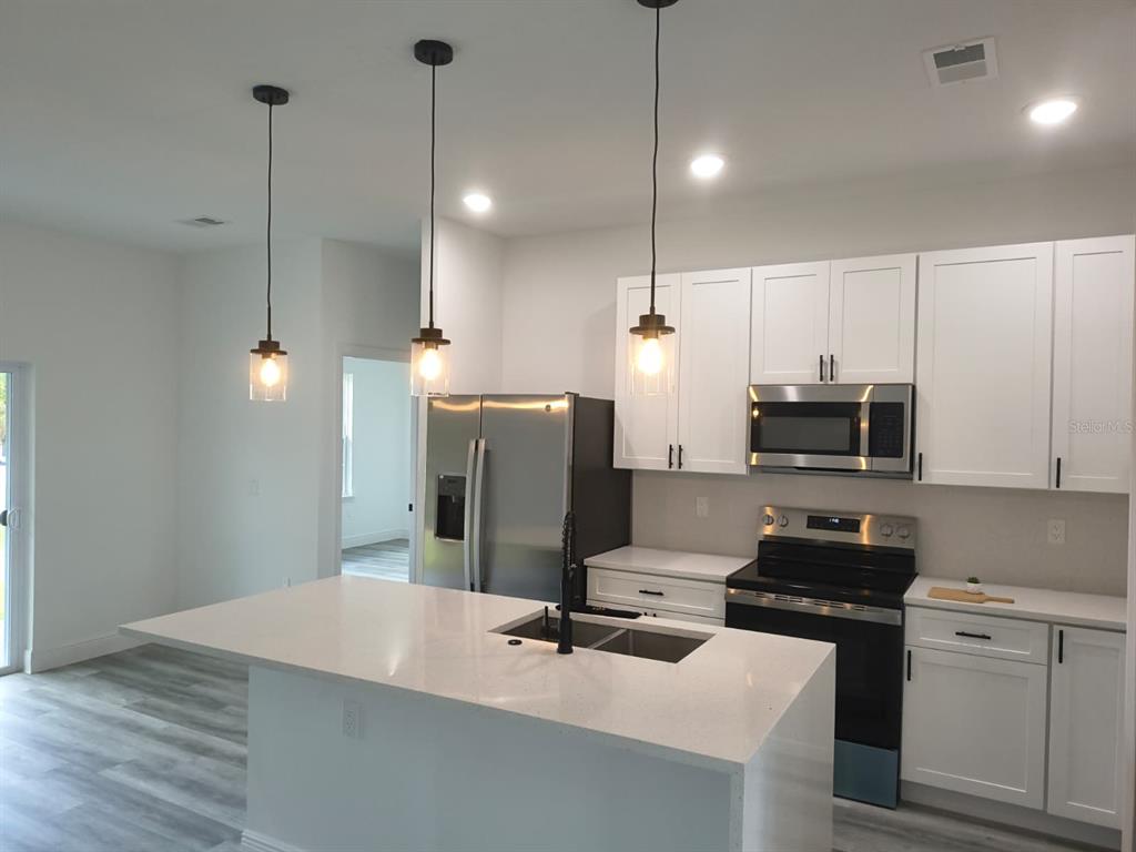 A modern kitchen features white cabinets, stainless steel appliances, and a quartz-topped island with pendants — 171 MARION OAKS TRAIL, OCALA, FL