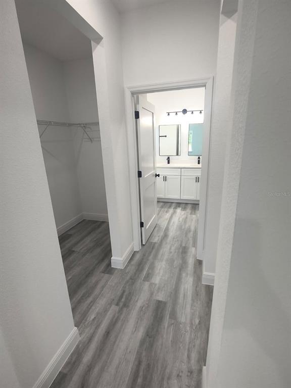 A hallway with wood-look flooring leads to a bathroom with white cabinets and dual mirrors — 171 MARION OAKS TRAIL, OCALA, FL