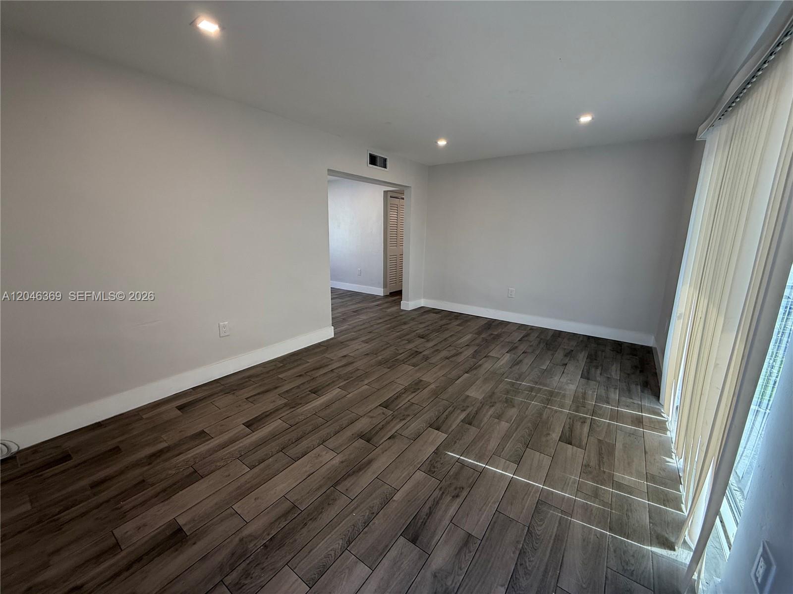 An empty room features light gray walls, recessed ceiling lights, and dark wood-look tile flooring — 12th Street SE 12th St # 837, Hialeah FL 33010, HIALEAH, FL
