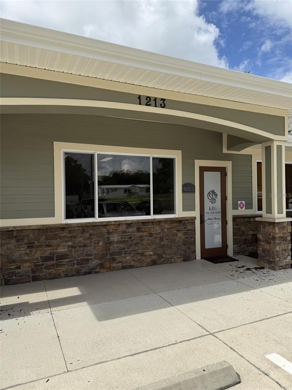 The exterior of a commercial building features tan siding, stone veneer, and a glass door — 1213 W MILLER STREET, FRUITLAND PARK, FL