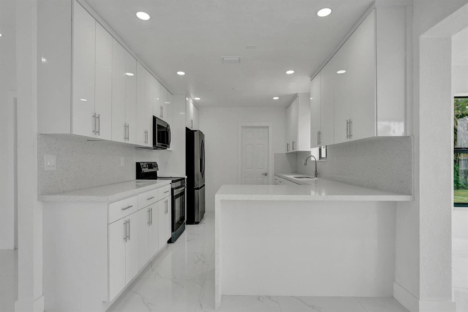 A modern kitchen features white cabinets, quartz countertops, stainless steel appliances, and white tile flooring — 2301 Alcazar Drive, Miramar FL 33023, MIRAMAR, FL