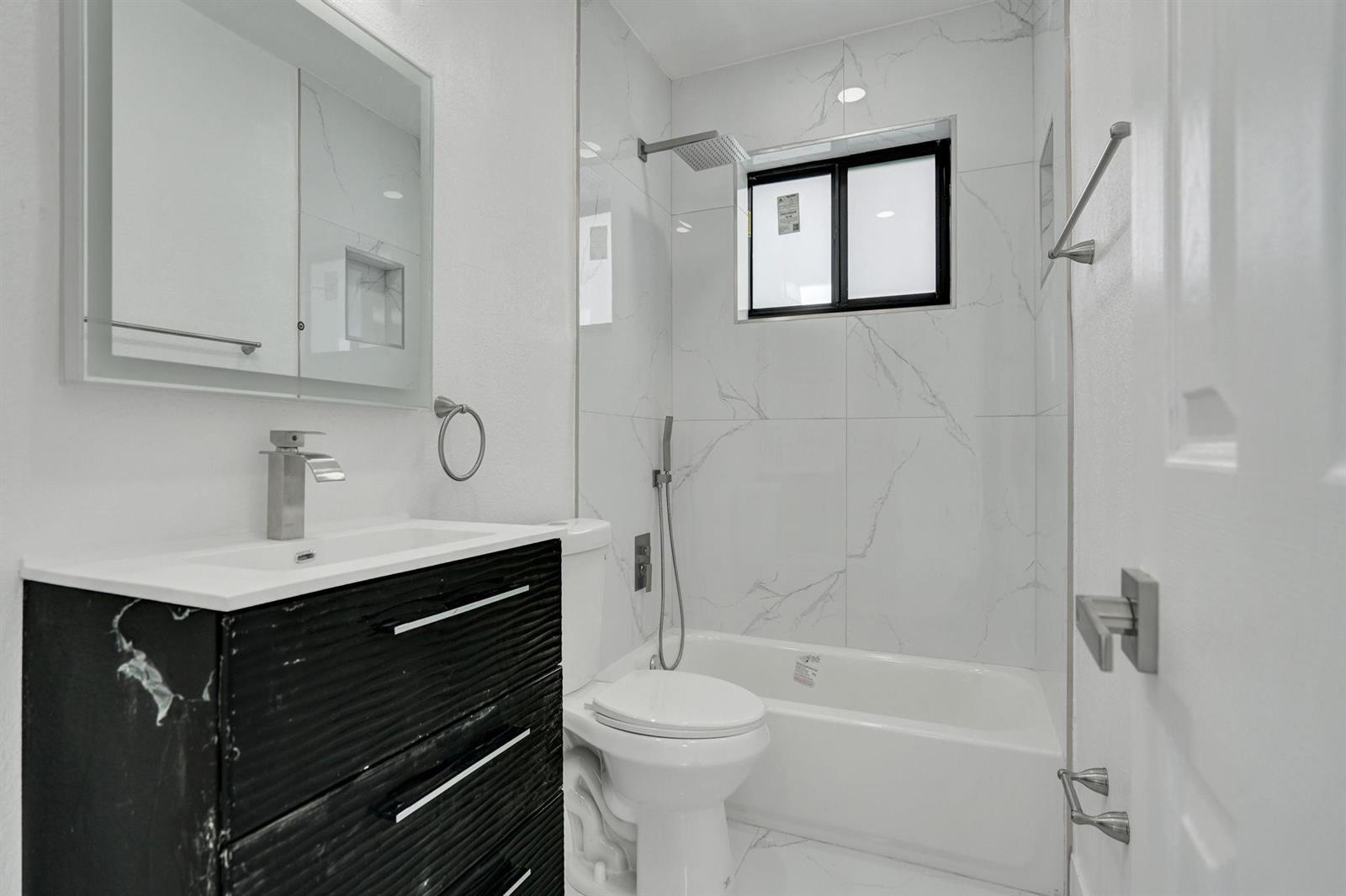 A bathroom features a black vanity, a white toilet, and a bathtub with marble-look tile — 2301 Alcazar Drive, Miramar FL 33023, MIRAMAR, FL