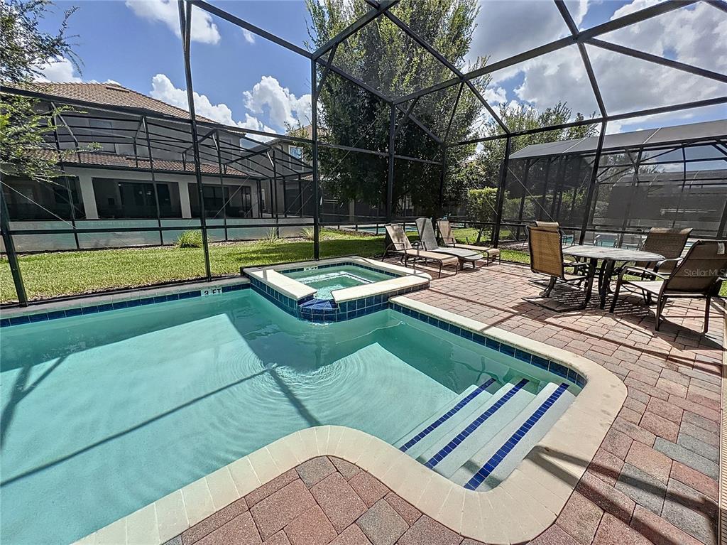 A screened-in patio features a swimming pool with an attached spa and brick pavers — 1453 MYRTLEWOOD STREET, DAVENPORT, FL