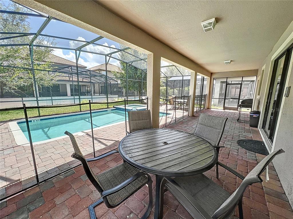 A covered patio features a dining set, brick pavers, and a screened-in pool area — 1453 MYRTLEWOOD STREET, DAVENPORT, FL