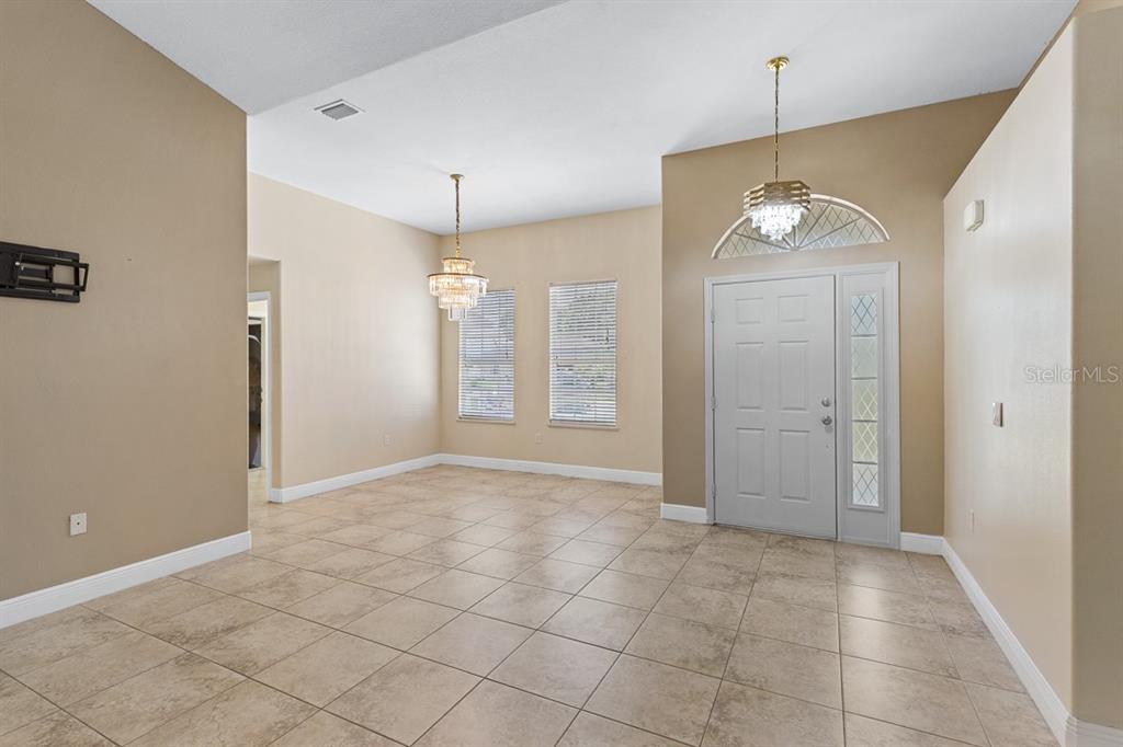 An entryway with beige walls, tile flooring, two crystal chandeliers, and a white front door — 2326 JACKSON DRIVE, SEBRING, FL
