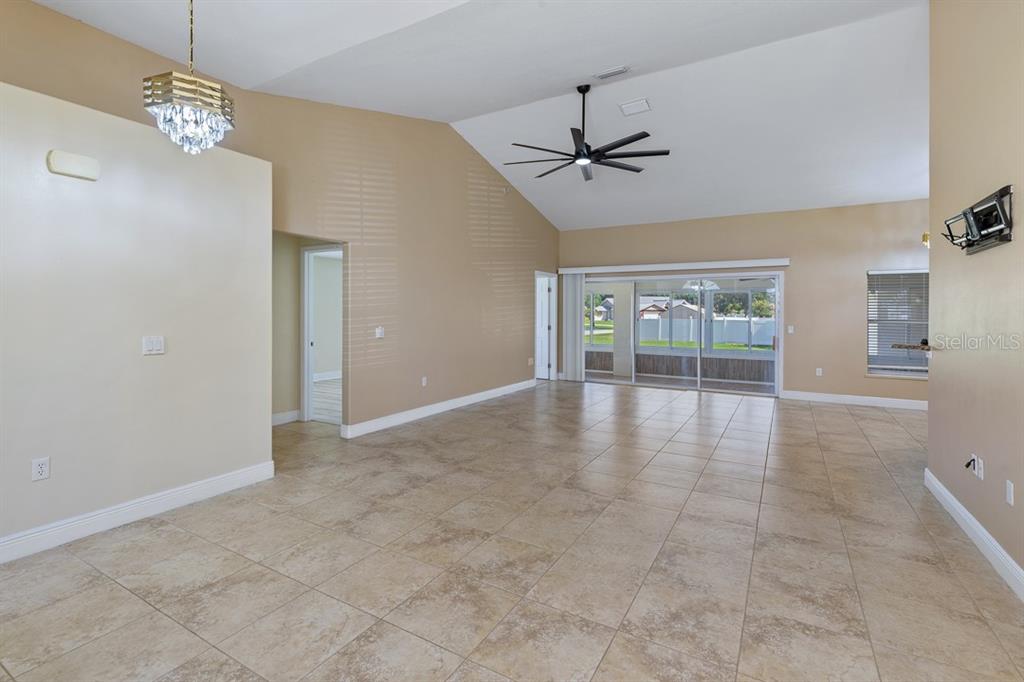 An open-concept living area features tan tile floors, vaulted ceilings, and a sliding glass door — 2326 JACKSON DRIVE, SEBRING, FL