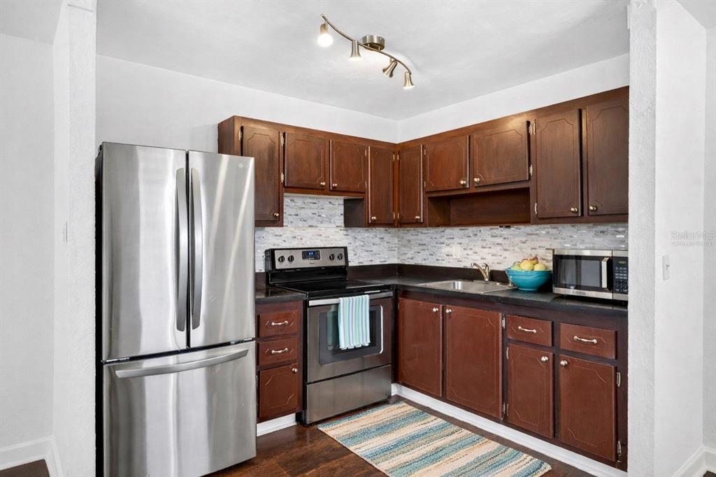 A kitchen features dark wood cabinets, stainless steel appliances, and a light-colored tile backsplash — 1801 BEDFORD LANE UNIT 27, SUN CITY CENTER, FL