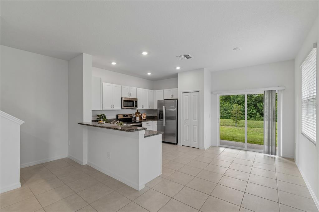 A kitchen with white cabinets, stainless steel appliances, and a breakfast bar overlooks a backyard — 222 TULIP BANDED WAY, RUSKIN, FL