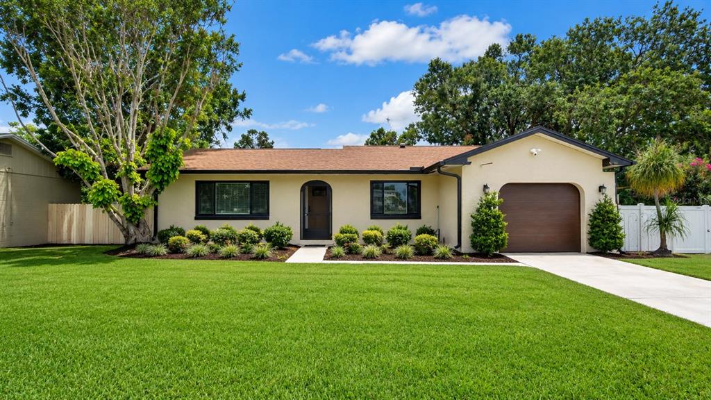 A single-story house with a tan exterior, dark trim, a brown garage door, and green lawn — 7577 DOCKSIDE STREET, WINTER PARK, FL