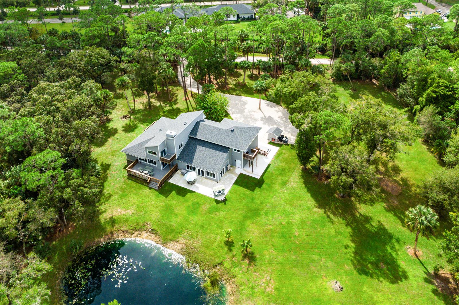 An aerial view of a gray house with a deck, patio, and pond — 12151 Old Indiantown Road, Jupiter FL 33478, JUPITER, FL