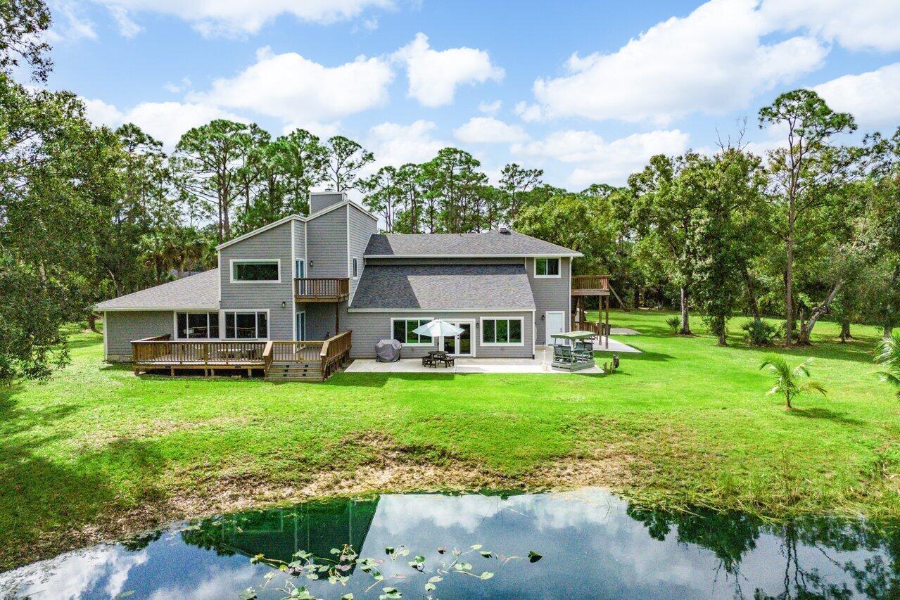 A gray two-story house with a wooden deck overlooks a pond and a grassy yard — 12151 Old Indiantown Road, Jupiter FL 33478, JUPITER, FL