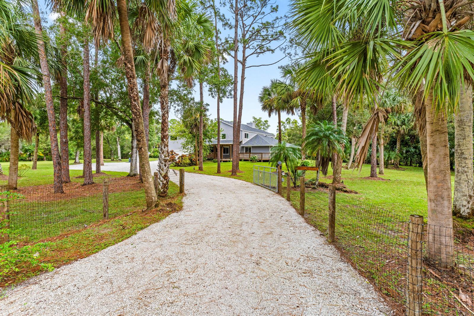 A gravel driveway leads through a wooded yard toward a two-story gray house — 12151 Old Indiantown Road, Jupiter FL 33478, JUPITER, FL