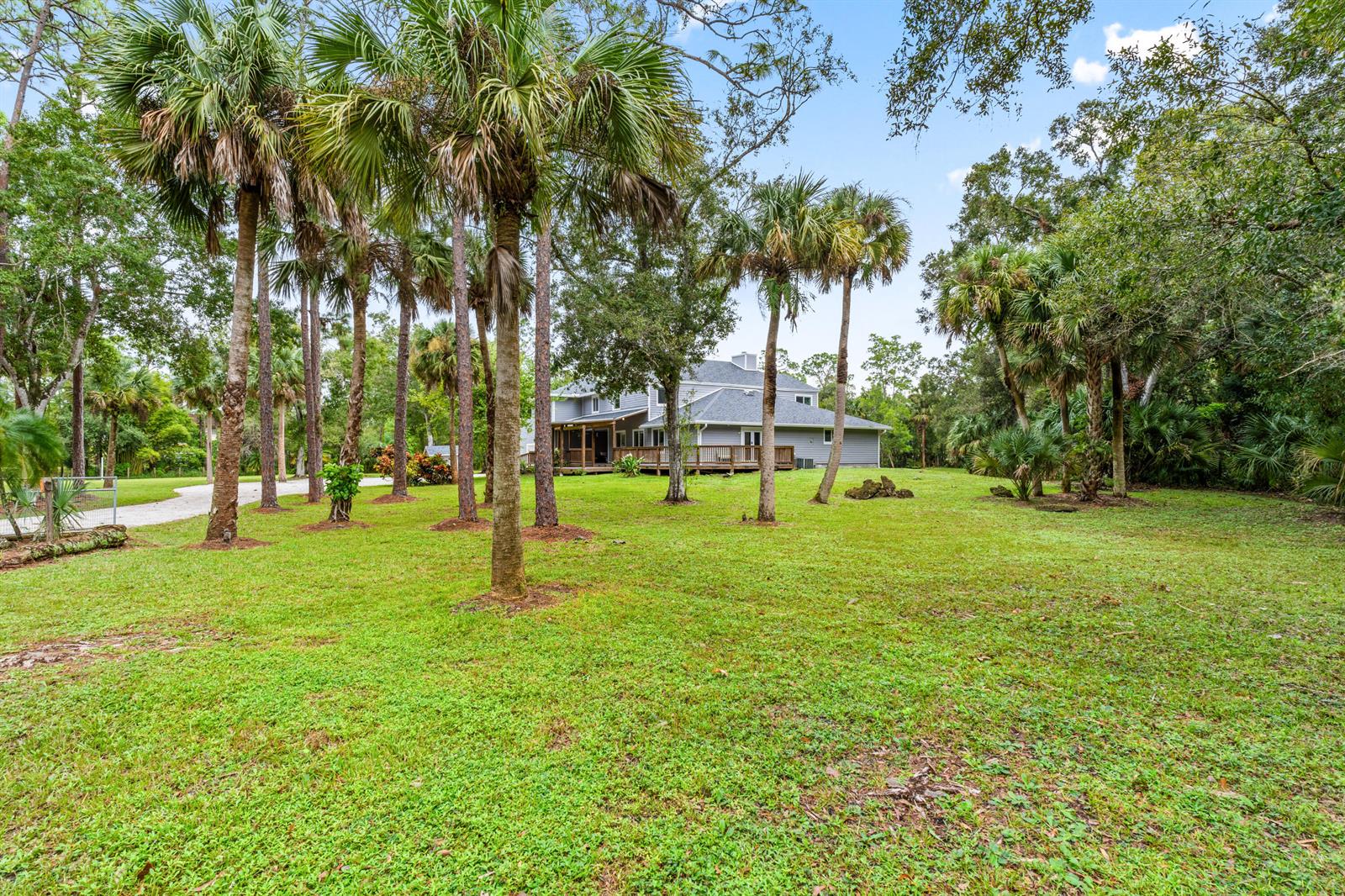 A two-story gray house with a wooden deck sits on a grassy, tree-filled lot — 12151 Old Indiantown Road, Jupiter FL 33478, JUPITER, FL