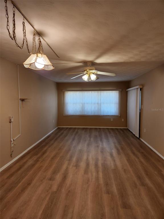 An empty room features wood-look flooring, a ceiling fan, and a hanging light fixture — 3100 HARBOR BOULEVARD UNIT 102, PORT CHARLOTTE, FL