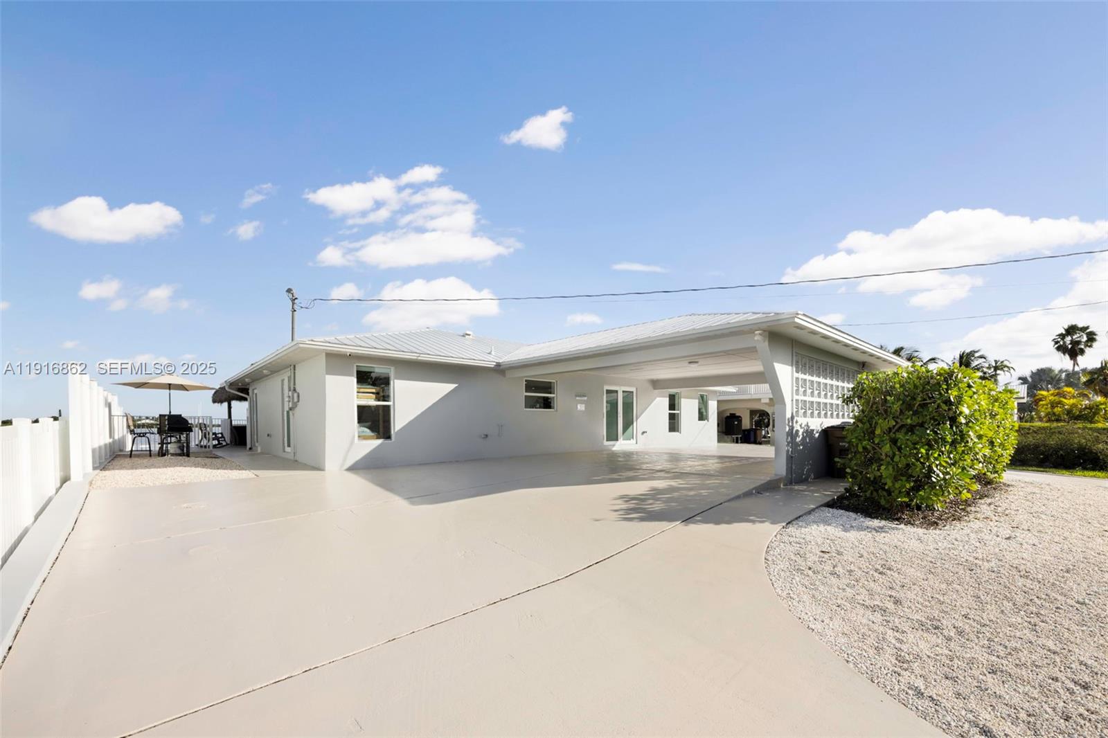 A light-colored house features a large concrete driveway, a covered carport, and a patio area — 1733 Sunrise Dr, Big Pine FL 33043, BIG PINE, FL