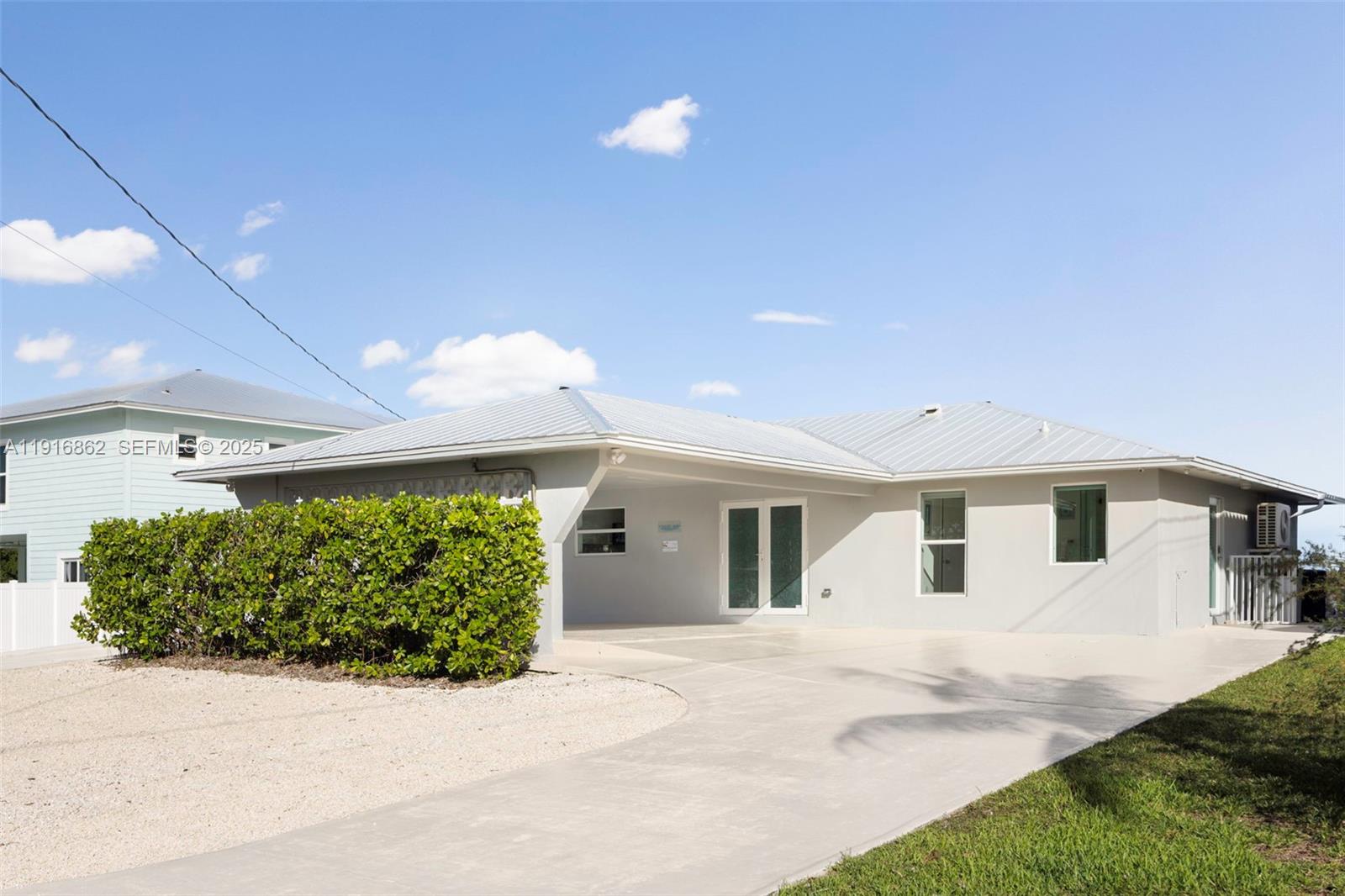 A single-story house with a metal roof, a concrete driveway, and a large privacy hedge — 1733 Sunrise Dr, Big Pine FL 33043, BIG PINE, FL