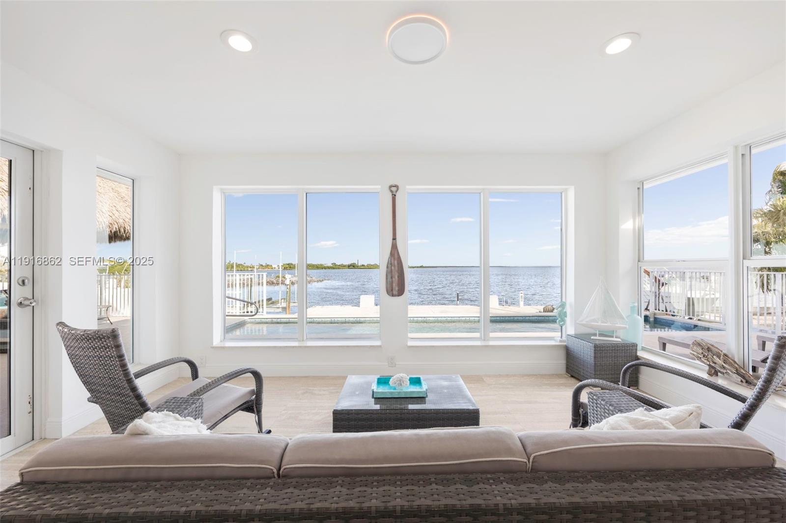 A sunroom with wicker furniture overlooks a swimming pool and a waterfront dock — 1733 Sunrise Dr, Big Pine FL 33043, BIG PINE, FL