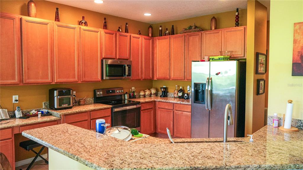 A kitchen features wood cabinets, granite countertops, stainless steel appliances, and a breakfast bar — 4055 BEACON RIDGE WAY, CLERMONT, FL