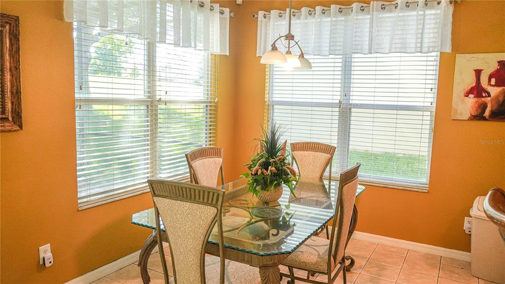 A dining area with a glass-topped table, four chairs, and windows with white blinds — 4055 BEACON RIDGE WAY, CLERMONT, FL