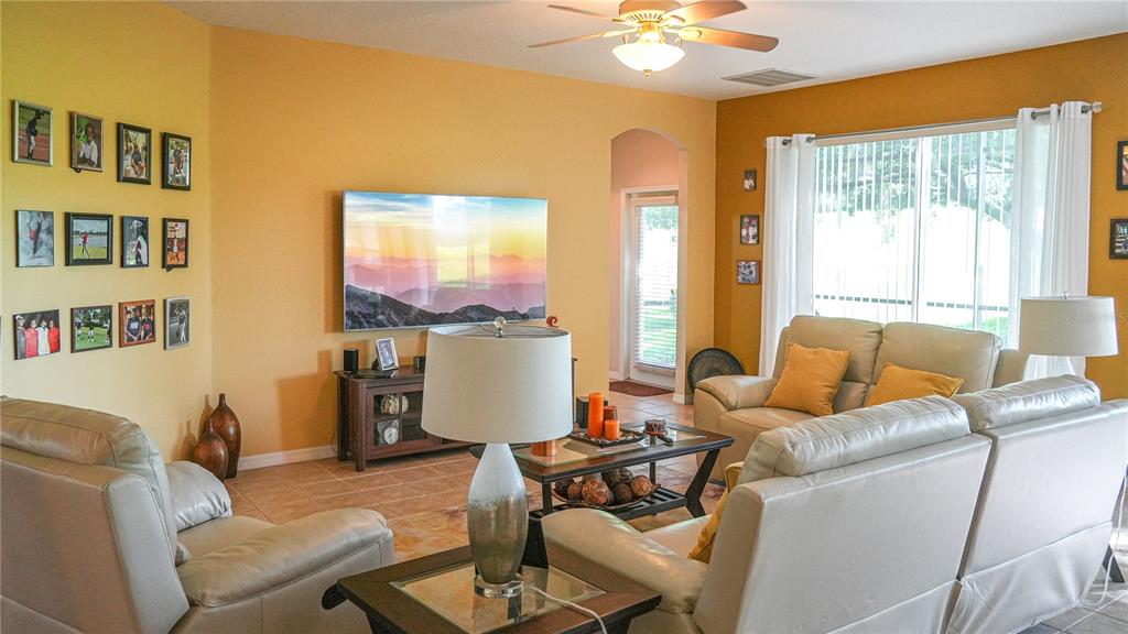 A living room features a wall-mounted television, beige leather furniture, and a gallery wall — 4055 BEACON RIDGE WAY, CLERMONT, FL