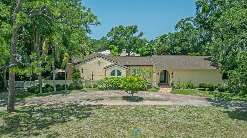 A single-story tan house with a dark roof sits behind a curved driveway and trees — 1330 INDIAN ROCKS ROAD, BELLEAIR, FL
