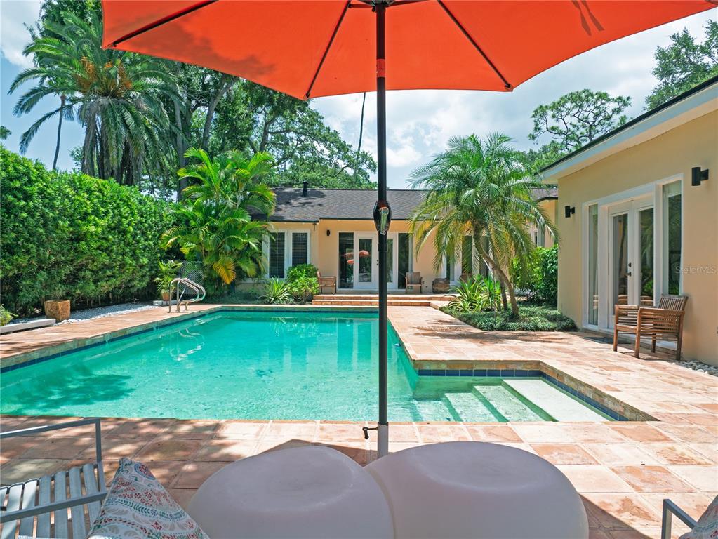 A swimming pool with a patio and orange umbrella sits in a backyard with palm trees — 1330 INDIAN ROCKS ROAD, BELLEAIR, FL