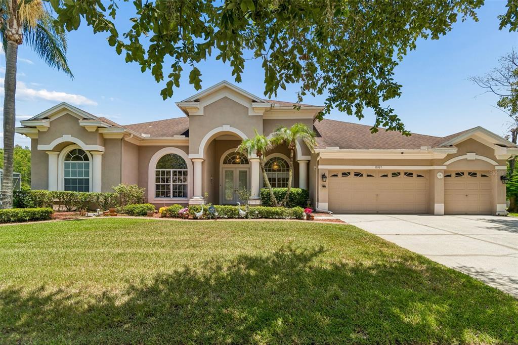 A single-story suburban house with a tan stucco exterior, arched entryway, and three-car garage — 18107 EMERALD BAY STREET, TAMPA, FL