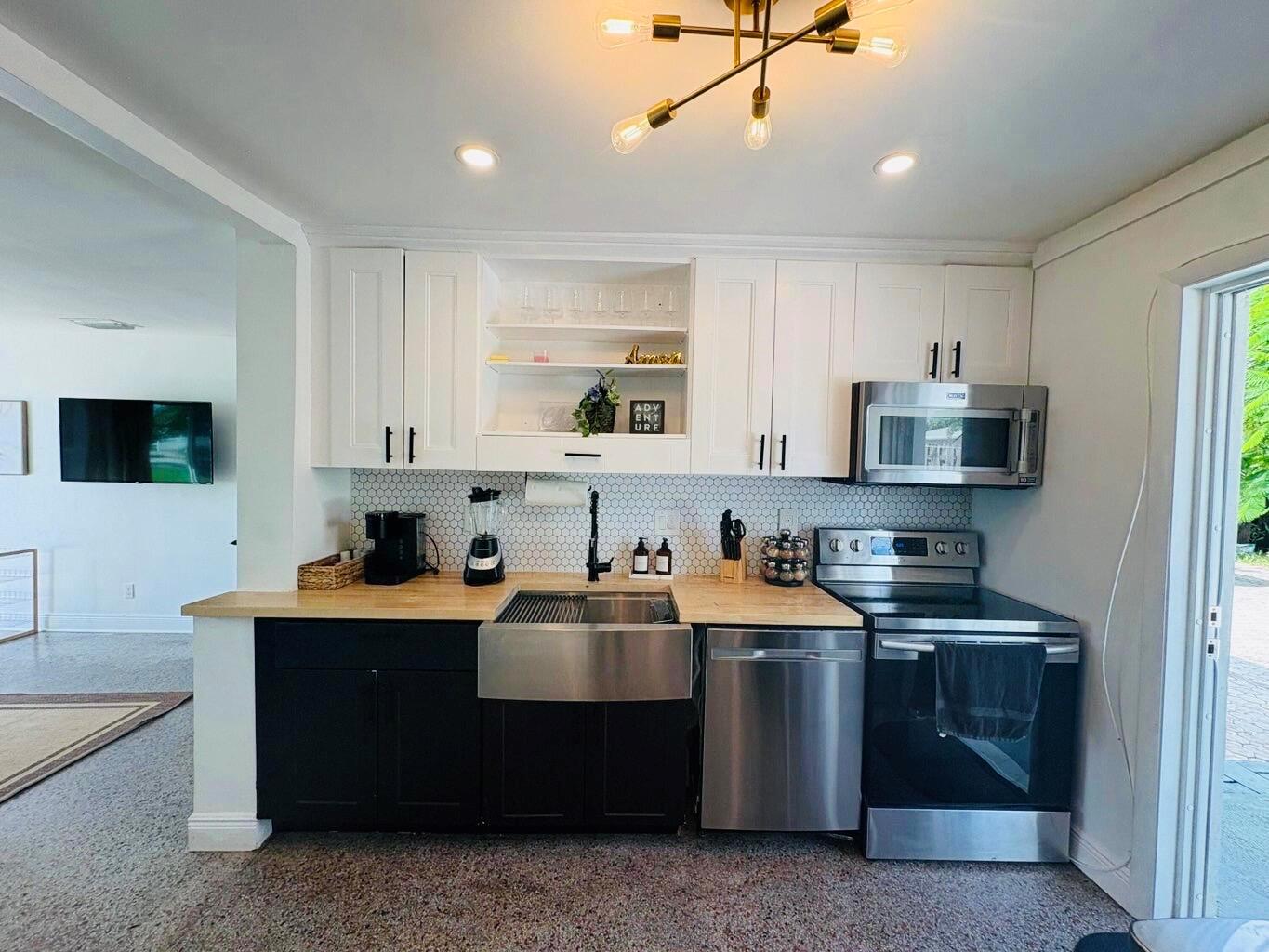 A kitchen features white upper cabinets, black lower cabinets, a farmhouse sink, and stainless appliances — 2711 NE 11th Terrace, Pompano Beach FL 33064, POMPANO BEACH, FL