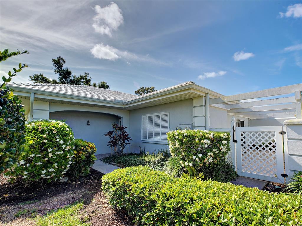 A single-story house exterior with a white lattice gate, manicured shrubs, and a tiled roof — 262 CERROMAR WAY S UNIT 53, VENICE, FL