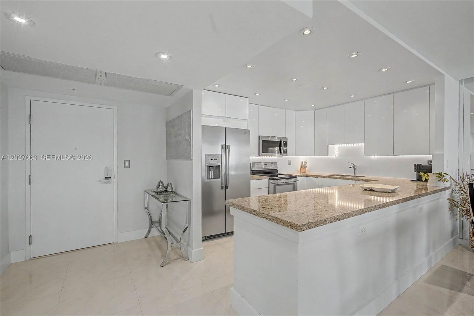 A modern kitchen features white cabinetry, stainless steel appliances, and a granite-topped breakfast bar — 2301 Collins Ave # 1210, Miami Beach FL 33139, MIAMI BEACH, FL